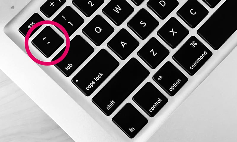 Englische Tastatur mit der Tilde-Taste farblich hervorgehoben.